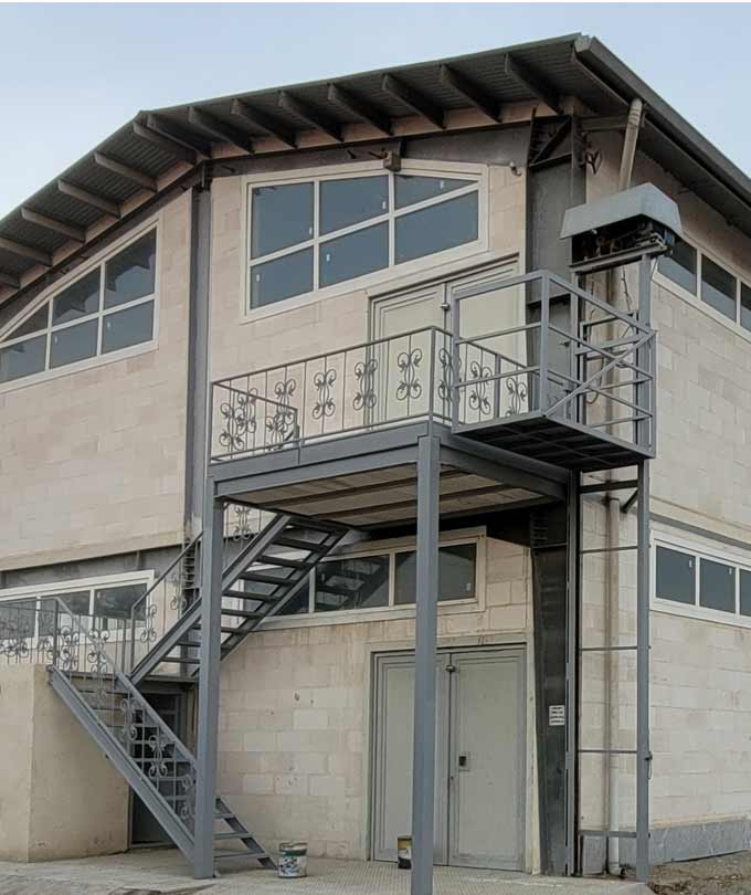Exterior view of DARKAR lighting factory building with industrial staircase, steel balcony, and modern stone facade