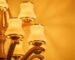 Close-up of a luxurious wooden chandelier with curved arms and gold-trimmed frosted glass shades, glowing warmly against a golden background
