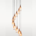 Ten-light spiral pendant lamp with cylindrical frosted glass and carved wooden tops – Checkmark Model 38-11 – ideal for tall spaces, stairs, and modern rustic lobbies
