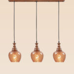 Horizontal triple pendant light with carved wood tops and amber-patterned globe shades – Checkmark Model 61h3 – rustic linear hanging light for kitchen and dining spaces