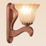 Wooden wall sconce light with light curved arm and fluted amber glass shade – distributed by Checkmark, crafted by DARKAR Lighting Industries.