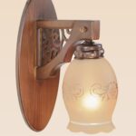 Wooden wall sconce light with ornate side panel and floral-etched frosted glass shade – distributed by Checkmark, crafted by DARKAR Lighting Industries.