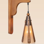 Rustic wooden wall sconce light with hanging tapered shade and decorative cutouts – distributed by Checkmark, crafted by DARKAR Lighting Industries.