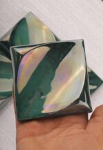 Detail view of a handcrafted ceramic decorative square tile showing layered glaze and ceramic texture